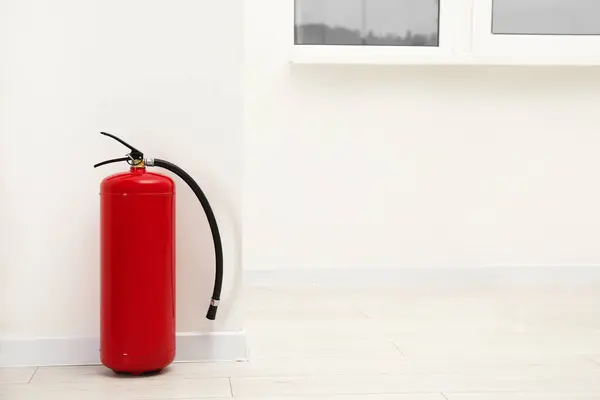 stock image Fire extinguisher on floor near light wall indoors, space for text