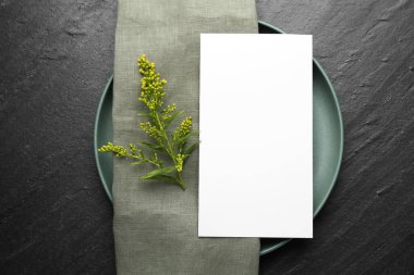 Boş menü, tabak, peçete ve çiçek dekoru siyah masanın üstünde. Tasarım için model