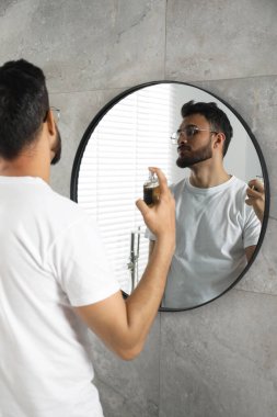 Adam evin içinde aynanın yanına lüks parfüm sıkıyor.