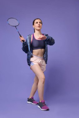 Mor arka planda raketle badminton oynayan genç bir kadın.