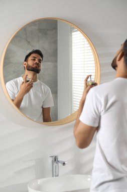 Adam evin içinde aynanın yanına lüks parfüm sıkıyor.
