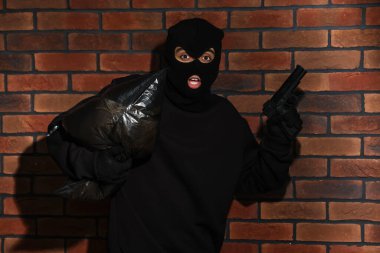 Kırmızı tuğla duvara karşı silahlı, kar maskeli duygusal bir hırsız.