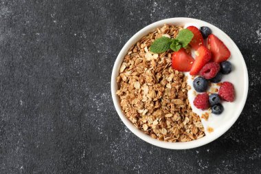 Lezzetli granola, böğürtlenli yoğurt ve koyu dokulu masa, üst manzara. Metin için boşluk