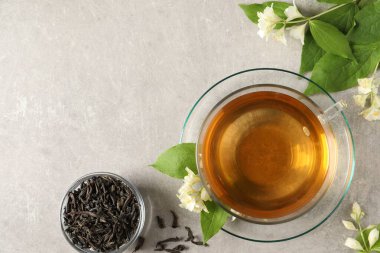 Aromatik yasemin çayı bardakta, çiçekler ve kuru yapraklar açık gri masada, düz yerde. Metin için boşluk