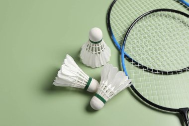 Yeşil arka planda badminton mekikleri ve raketler var. Metin için boşluk