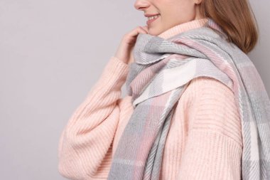 Woman in warm scarf on gray background, closeup. Space for text