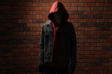 Kapüşonlu hırsız kırmızı tuğladan duvara karşı