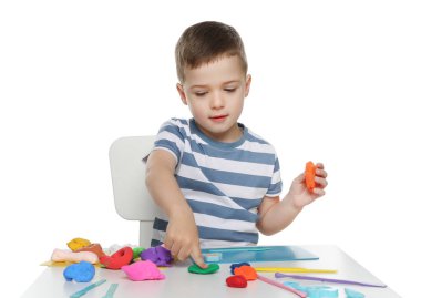 Beyaz arka planda masada hamurla heykel yapan küçük çocuk.