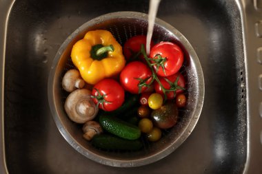 Farklı sebzeleri musluk suyuyla yıkamak lavabonun içindeki metal kevgir, üst manzara.