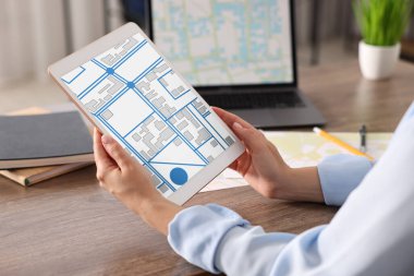 Tablette kadastro haritasıyla çalışan bir kadın ve masadaki dizüstü bilgisayar, yakın plan.
