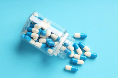 Açık mavi arka planda dağınık antibiyotik haplar ve şişe, üst manzara. Tıbbi tedavi
