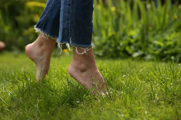 Woman walking barefoot on green grass outdoors, closeup