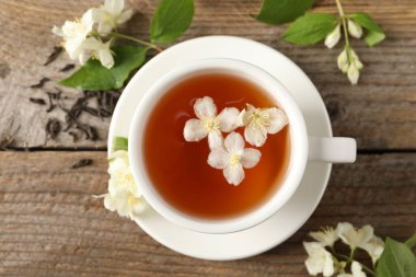 Aromatik yasemin çayı fincanda, çiçekler ve kuru yapraklar ahşap masada, üst manzara