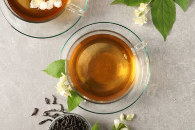Aromatik yasemin çayı bardaklarda, çiçekler ve kuru yapraklar açık gri masada, düz yatıyordu.