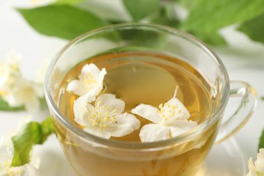 Aromatik yasemin çayı fincanda, çiçekler ve yeşil yapraklar masada, yakın çekim