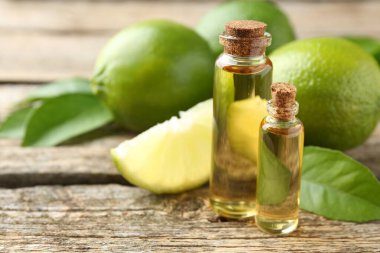 Temel yağlar şişelerde, limonlarda ve yeşil yapraklar ahşap masada, yakın plan.