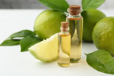 Temel yağlar şişelerde, limonlarda ve yeşil yapraklar beyaz masada, yakın plan