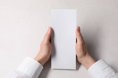 Woman holding blank card at white table, top view. Mockup for design