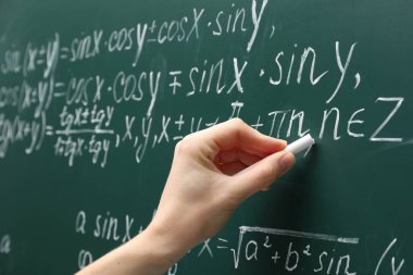 Teacher writing down math equation on green board, closeup