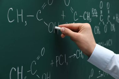 Teacher writing chemical formulas with chalk on green chalkboard, closeup