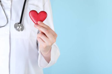 Açık mavi arka planda kırmızı kalpli doktor, yakın plan. Metin için boşluk