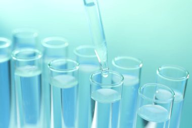 Turkuaz arka planda pipetten test tüpüne sıvı damlatılıyor.