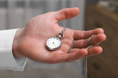 Man holding chain with elegant pocket watch on blurred background, closeup