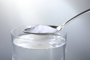 Açık gri arka planda, su bardağının üzerinde kabartma tozu bulunan kaşık, yakın plan.