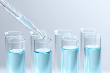 Işık arka planında pipetten test tüpüne sıvı damlatılıyor, yakın plan