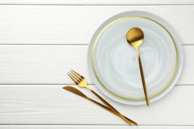 Beyaz ahşap masa üzerine çatal bıçak ve tabak döşenmiş şık bir ortam. Metin için boşluk