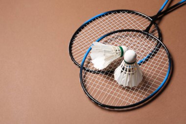 Tüylü badminton mekikleri ve raketleri kahverengi arka planda, metin için boşluk