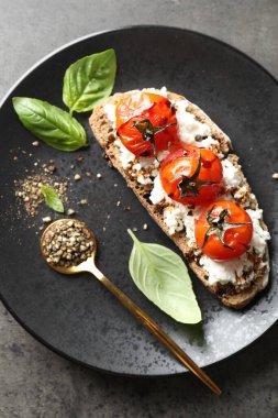 Lezzetli ricotta bruschetta, güneşte kurutulmuş domates, sos, fesleğen ve öğütülmüş biber, gri desenli masa, üst manzara.