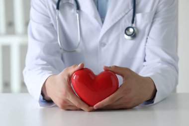 Klinikteki beyaz masada kırmızı kalpli doktor, yakın plan.