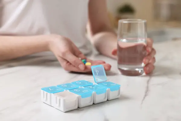 stock image Woman with pills, organizer and glass of water at white marble table, selective focus