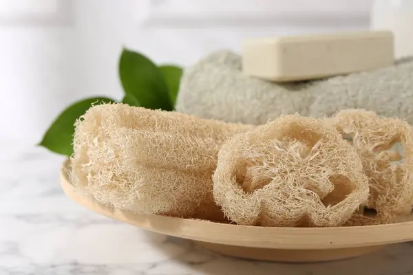 stock image Loofah sponges, soap, towel and green leaves on white marble table, closeup