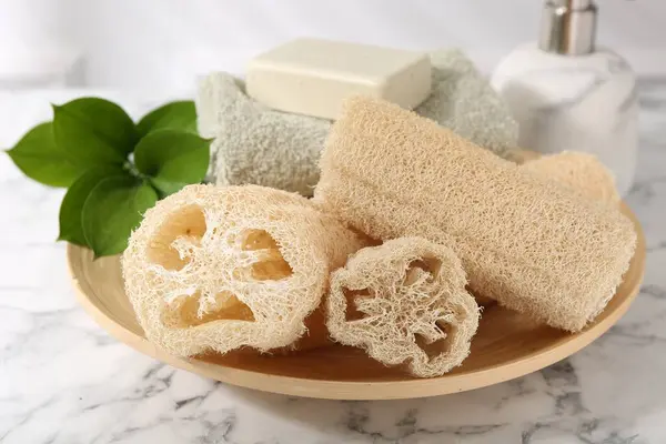 stock image Loofah sponges, soap, towel and green leaves on white marble table