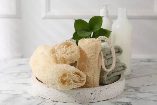 stock image Loofah sponges, towels, green leaves and cosmetic products on white marble table
