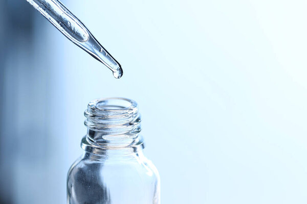 Dripping liquid from pipette into glass bottle on light blue background, closeup. Space for text