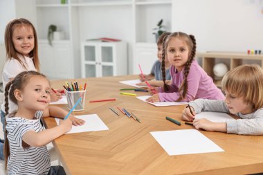 İçerideki ahşap masada resim yapan bir grup çocuk.