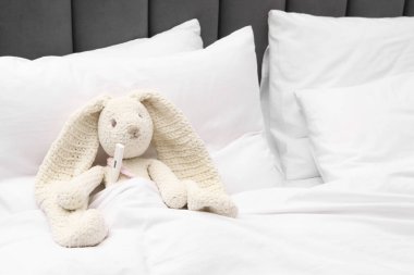 Yatağında battaniyenin altında termometresi olan sevimli oyuncak tavşan.