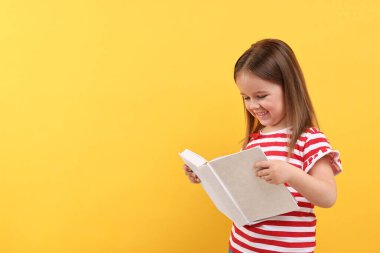 Turuncu arka plan üzerine kitap okuyan şirin küçük bir kız. Metin için boşluk