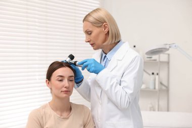Dermatoskoplu trikoloğum klinikte hastanın saçını inceliyor.