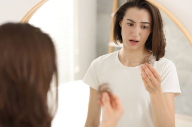 Stresli kadın içeride aynanın yanında saçlarını tutuyordu. Alopecia sorunu