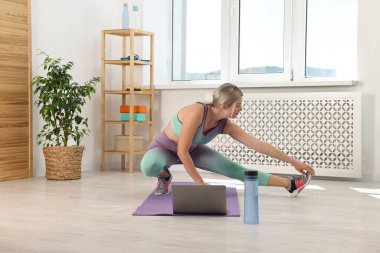 Online fitness trainer. Woman doing exercise near laptop at home