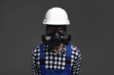 Gri arka planda gaz maskeli ve kasklı bir işçi.