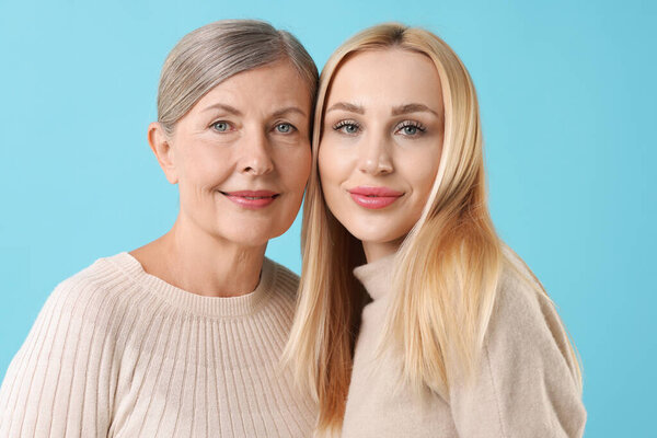 Family portrait of young woman and her mother on light blue background