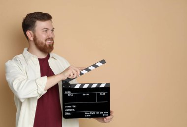 Making movie. Smiling man with clapperboard on beige background. Space for text