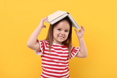 Turuncu arka plan üzerine açık kitabı olan sevimli küçük kız.