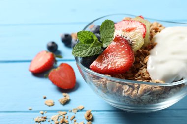 Böğürtlenli tahıl gevreği, yoğurt ve açık mavi ahşap masada nane, yakın plan.