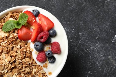 Lezzetli granola, böğürtlenli yoğurt ve koyu dokulu masa, üst manzara. Metin için boşluk